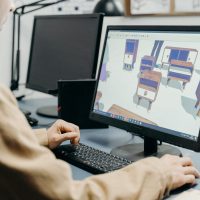 A product designer using a computer for 3D furniture modeling in an office setting.